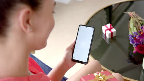 biracial teenage girl with gift having smartphone video call with copy space screen, slow motion