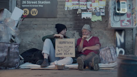 homeless friends holding sign and chatting as sitting in urban alley