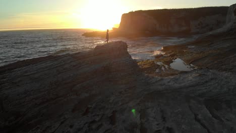 a slow moving drone flying forward and capturing a woman walking on a rock formation near panther beach, california