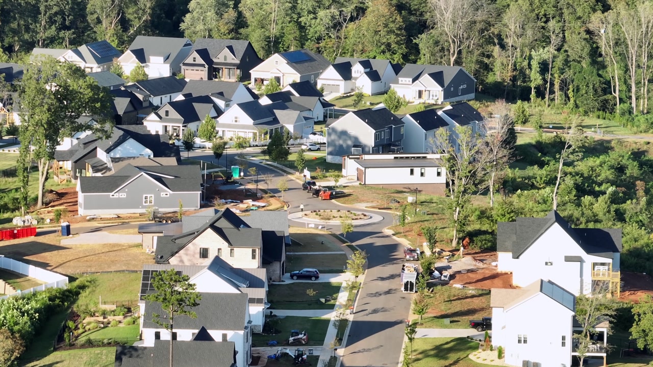 Aerial view of modern suburban neighborhood with new houses, streets, greenery and residential development surrounded by trees. Quiet and peaceful housing area.