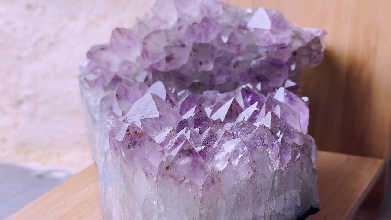 Grabación tomada con un movimiento de cámara ascendente de un cristal de amatista sobre una superficie de madera. Las puntas del cristal, de color púrpura con una base blanca, son claramente visibles