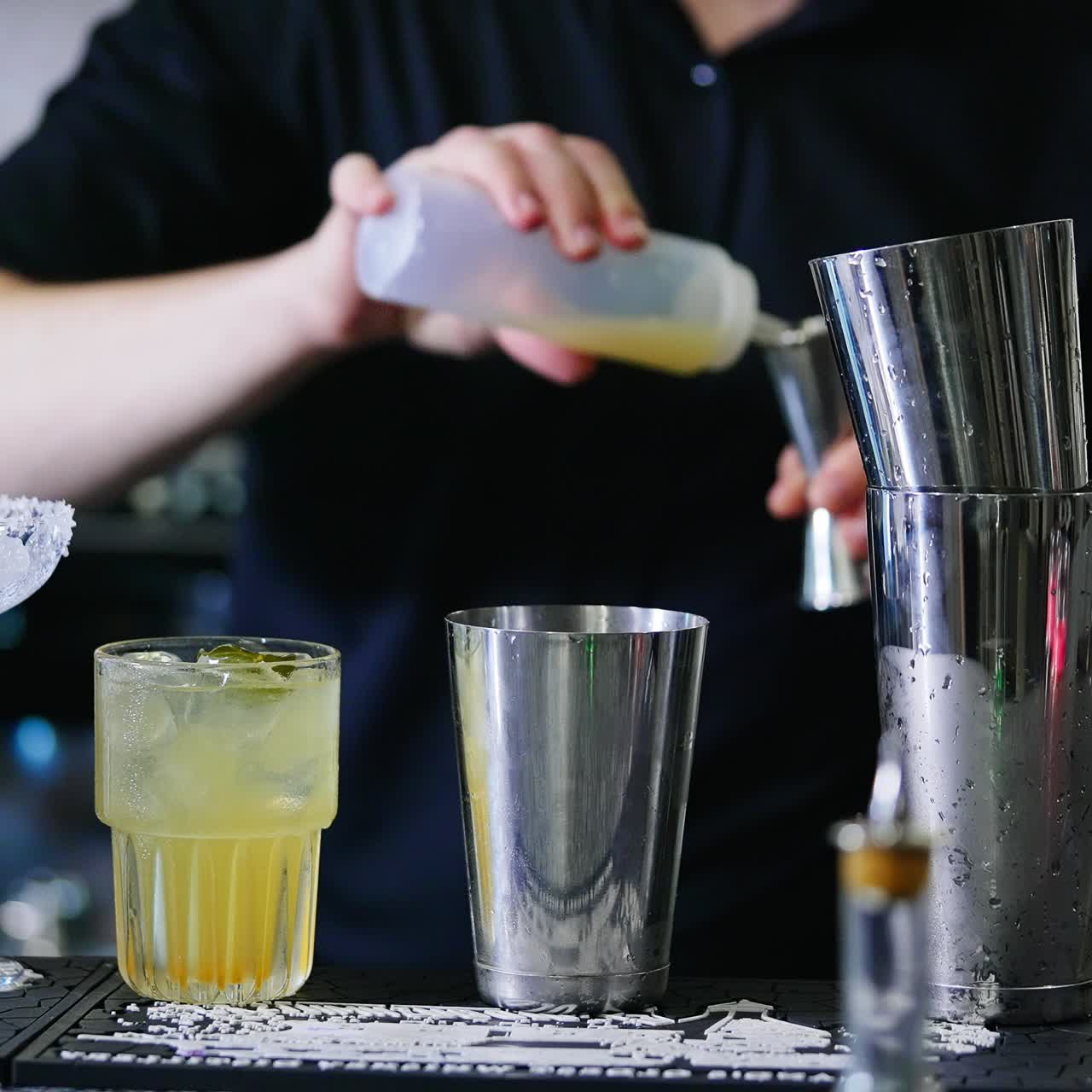 Bartender at working place at bar stand. Male barman preparing cocktails using metal glasses. Close up. Blurred backdrop