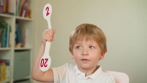 attentive little boy raises number fan during maths lesson