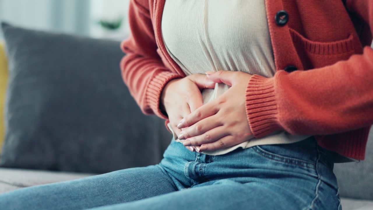 Stomach pain, woman hands and living room sofa