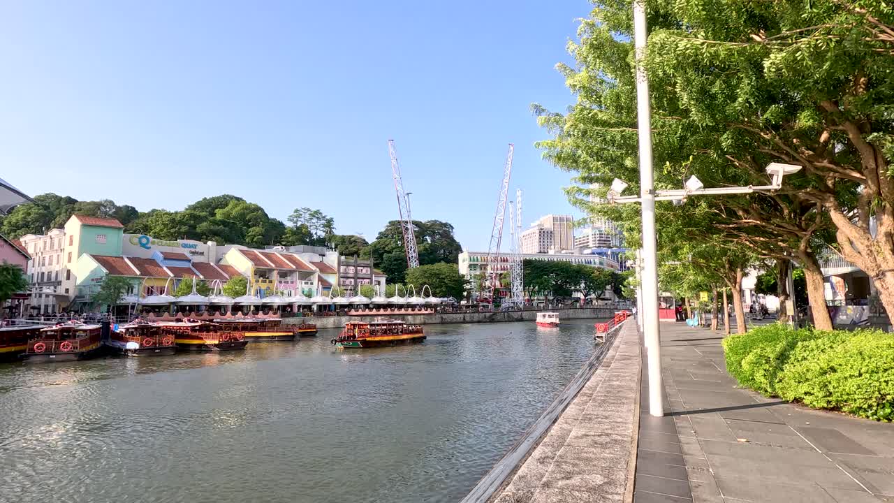 Camera pans along Clarke Quay riverfront, colorful buildings, boats, trees, and construction cranes visible