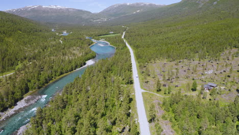 camper van travelling on a long narrow road with lush greenery and mountain river in stryn, norway