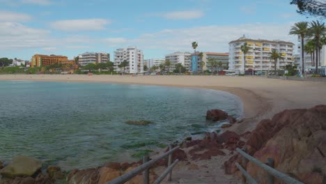 Ansicht-Des-Hauptstrandes-Von-Lloret-De-Mar-Mit-Den-Gebäuden-Im-Hintergrund-Und-Dem-Transparenten-Türkisblauen-Wasser-Des-Strandes,-Aufgenommen-In-4k-10bit-Ansicht-Des-Fanals-Strandes