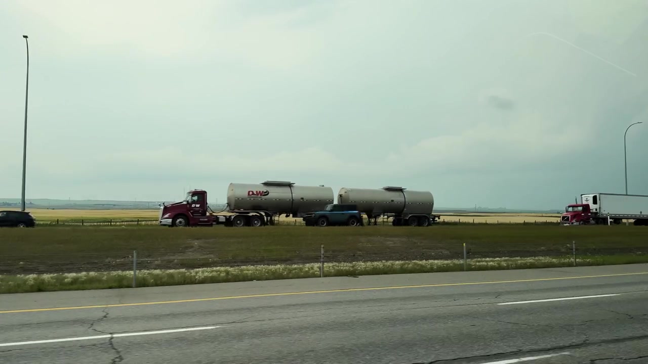 Veicoli viaggiano lungo un'autostrada divisa attraverso l'Alberta rurale pianeggiante sotto cieli nuvolosi.