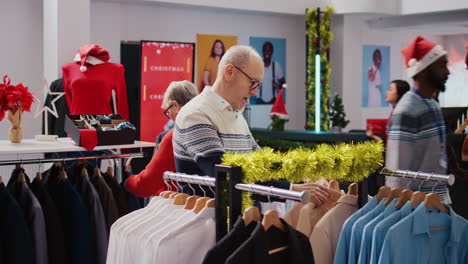 senescent customers browsing through clothing racks in festive ornate fashion boutique during xmas holiday season. aged couple happy after finding colorful blazers to gift at christmas family event