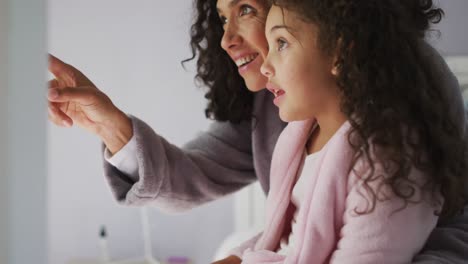 Glückliche-Gemischtrassige-Mutter-Und-Tochter,-Die-Im-Schlafzimmer-Sitzen-Und-Mit-Haaren-Spielen