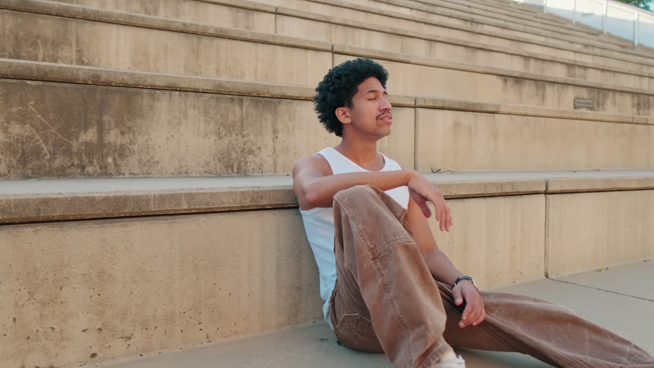 Thoughtful Young Man Sitting and Relaxing on Concrete Steps Outdoors