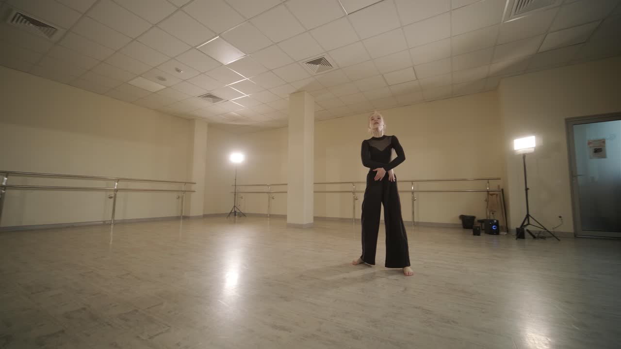 검은색 댄스웨어를 입은 젊은 발레 학생들이 나무 바닥과 벽에 장착된 바를 가진 넓은 발레 스튜디오에서 자세를 연습하는 그룹.