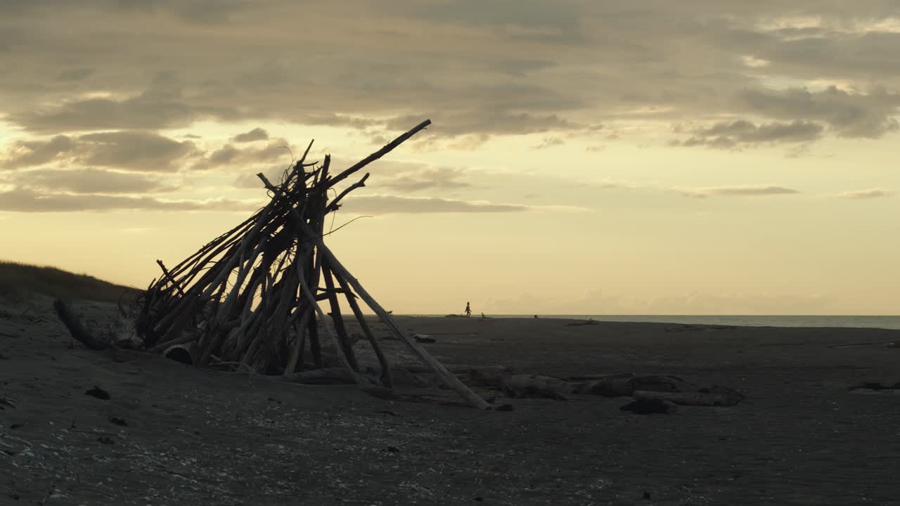 toma de fondo de la silueta de palos de madera para una fogata en la playa con una puesta de sol dorada