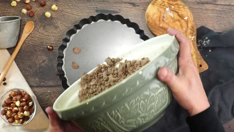 a delicious dessert, coffee hazelnut cream tart. made with espresso powder, chocolate crust and loaded with crushed hazelnut. hand mixing chocolate pie crust in a clear mixing bowl on a wooden table