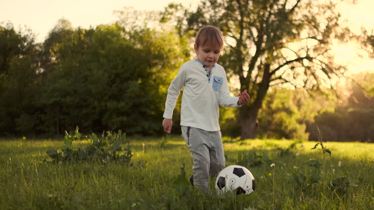 niño feliz corriendo con la pelota de fútbol corriendo al atardecer en el campo de verano.