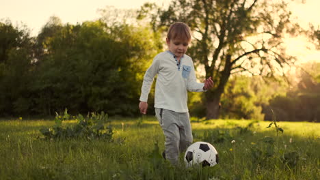 Glücklicher-Junge,-Der-Bei-Sonnenuntergang-Mit-Einem-Fußball-Auf-Einer-Sommerwiese-Läuft.