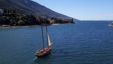 toma aérea de un velero histórico en el lago di garda con la costa al fondo en un día soleado