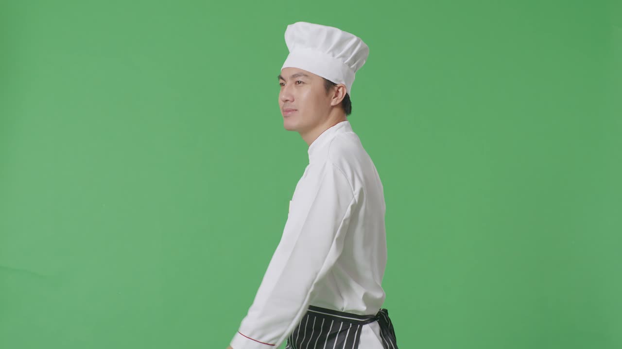 Vista laterale di uno chef asiatico che cammina e si guarda intorno in uno studio con sfondo green screen