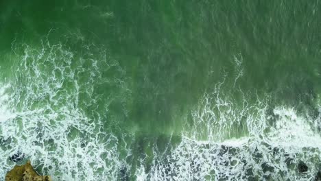 vista superior del océano verde turquesa mientras las olas rompen en las rocas en la costa de indonesia