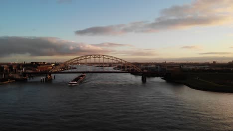 Container-ship-on-Noord-river-passing-under-bridge-at-sunset