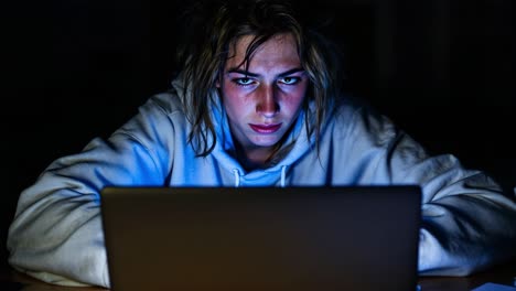 young person intensely focused on laptop in a dark room