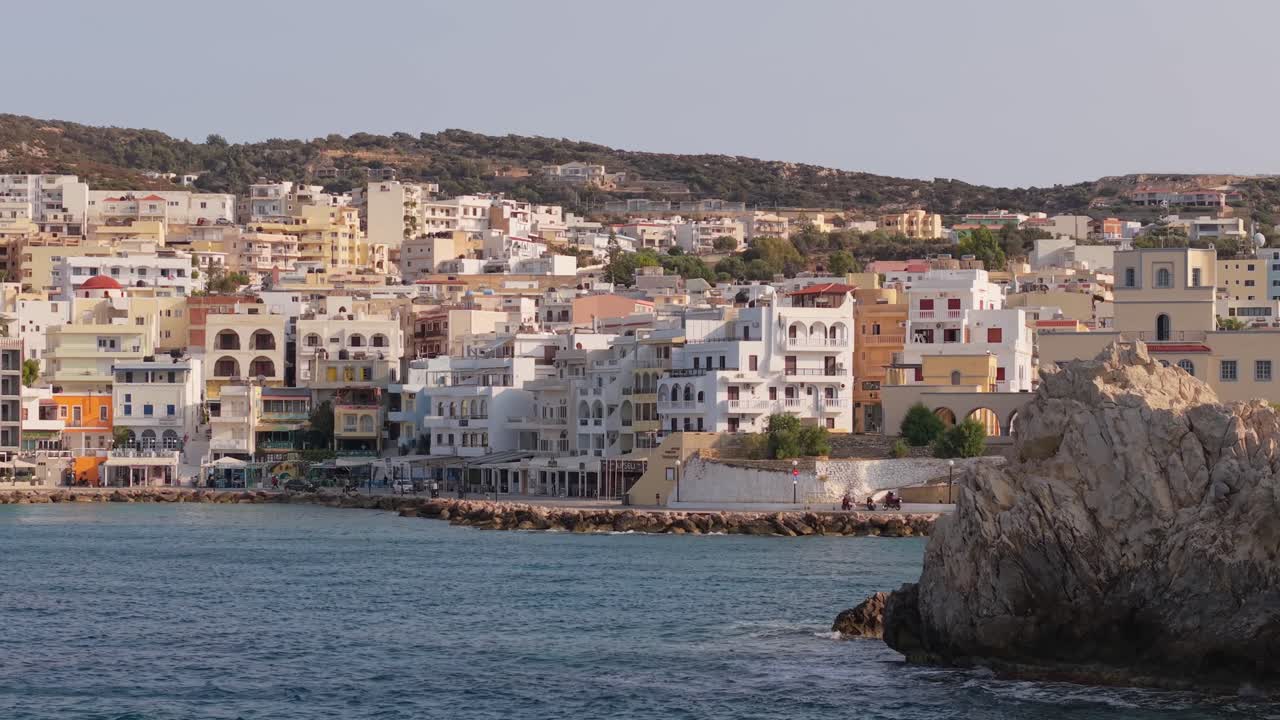 Drone footage revealing the beautiful seafront of Pigadia, Karpathos from the sea, showcasing the harbor, boats, and vibrant coastline under clear blue skies