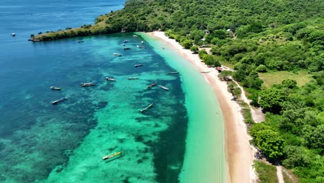 white sand beach with clear water, visible coral reefs and fishing boats on the beach