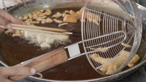 Street-food-vendor-deep-frying-Chinese-bread-stick-or-Youtiao-in-large-frying-pan-at-a-street-food-stall-in-Thailand