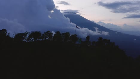 Aerial-view-of-a-volcanic-mountain-with-the-Indonesian-flag-waving-flag-on-a-hill-in-the-foreground