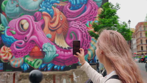 person holding cell phone taking a photo of mural in a city