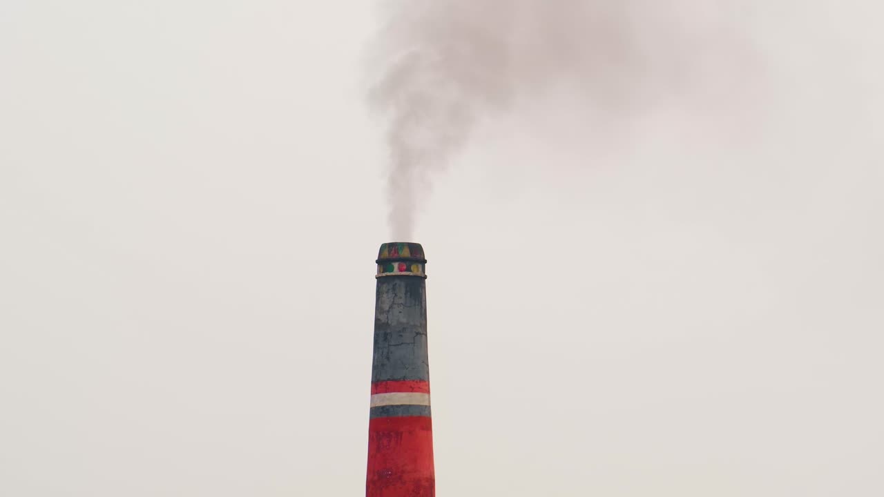 chimenea de campo de ladrillo rojo y negro que emite humo oscuro con un cielo gris en el fondo, bangladesh