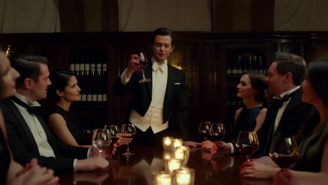 a group of elegantly dressed people making a toast with red wine at a formal dinner