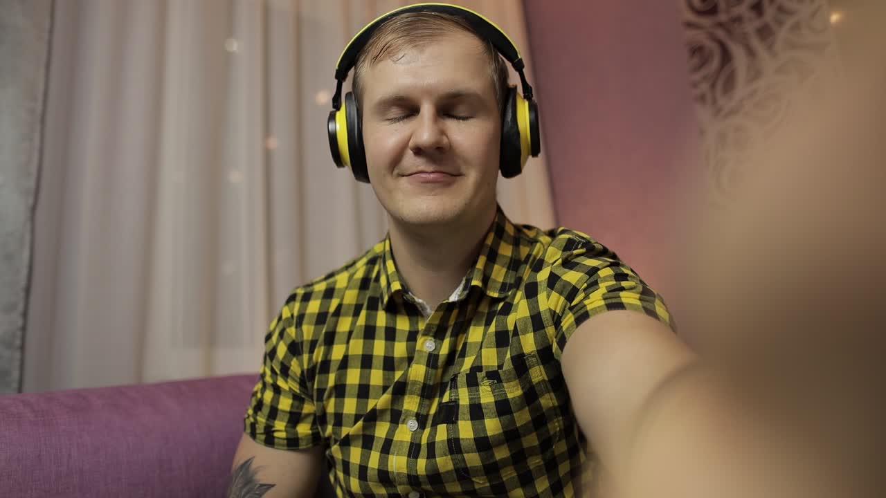 un hombre con una camisa amarilla a cuadros y auriculares sonríe para una selfie.