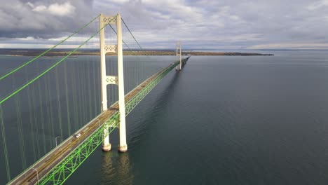 sun shines on mighty mac, mackinaw bridge while traffic is passing on a cloudy day, static aerial drone shot