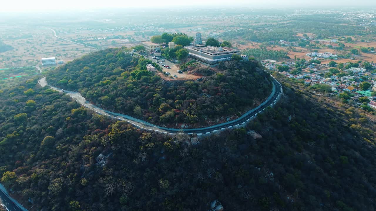 Aerial drone view of Sivanmalai temple majestically seated on a mountain top, overlooking a bustling village at its foothills, symbolizing spiritual devotion and scenic cultural heritage