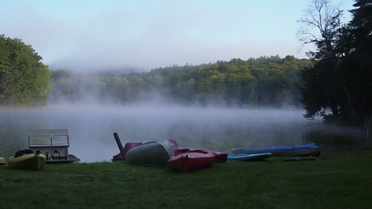 Canoes and kayaks at a pond with early morning mist floating over water