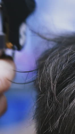 cu, slow motion: male hairdresser does trendy haircut to young customer with black hair using modern shiny golden machine in salon extreme closeup