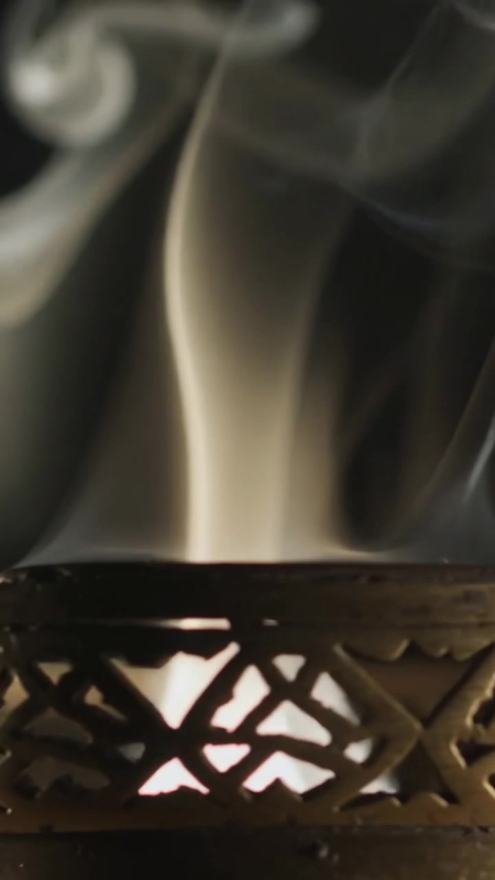 Vidéo verticale : Montrant un brûleur en métal orné, avec un treillis incandescent, émettant de la fumée de son cœur dans une pièce sombre.