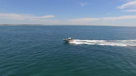 powerboat moviéndose rápido a través del océano en la soleada tarde seguimiento lateral aéreo