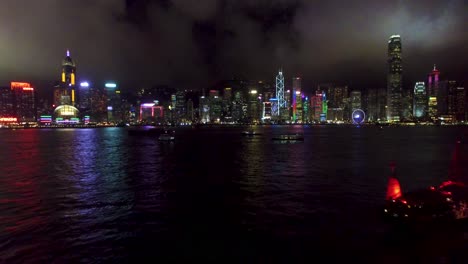 aerial view, hong kong night cityscape panorama and waterfront, shiny buildings on bay, drone shot