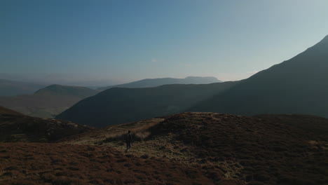 hiker walking through dead bracken towards misty mountain shadow in english lake district uk