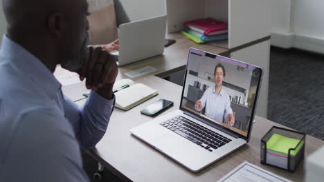 hombre mayor afroamericano teniendo una videollamada con un colega masculino en una computadora portátil en la oficina