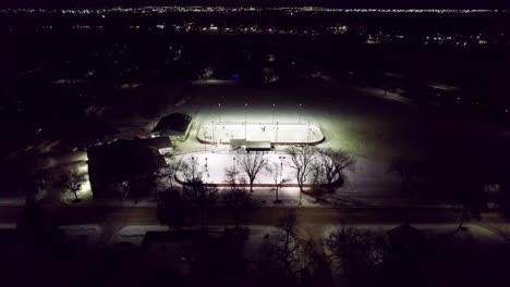 canadian winter night scene, outdoor hockey rinks illuminated by floodlight and city skyline, 4k drone shot