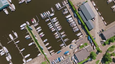 clockwise spiraling zoom in from zenithal perspective, showcasing dozens of sailboats docked in neat rows at the heeg harbor