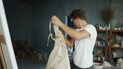 A-happy-successful-potter-in-a-studio-studio-finishes-his-working-day-in-the-background-of-a-shelf-with-his-products,-takes-off