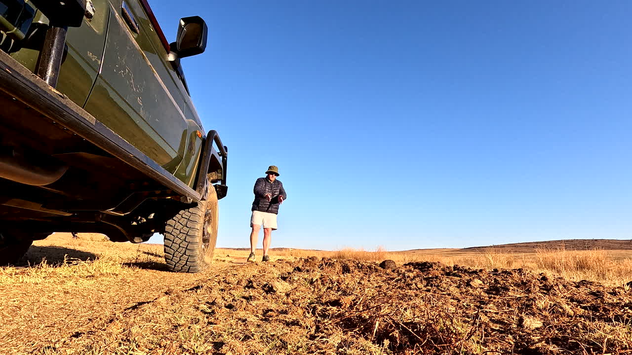 Low POV next to safari truck as field guide explains spoor tracking to tourists