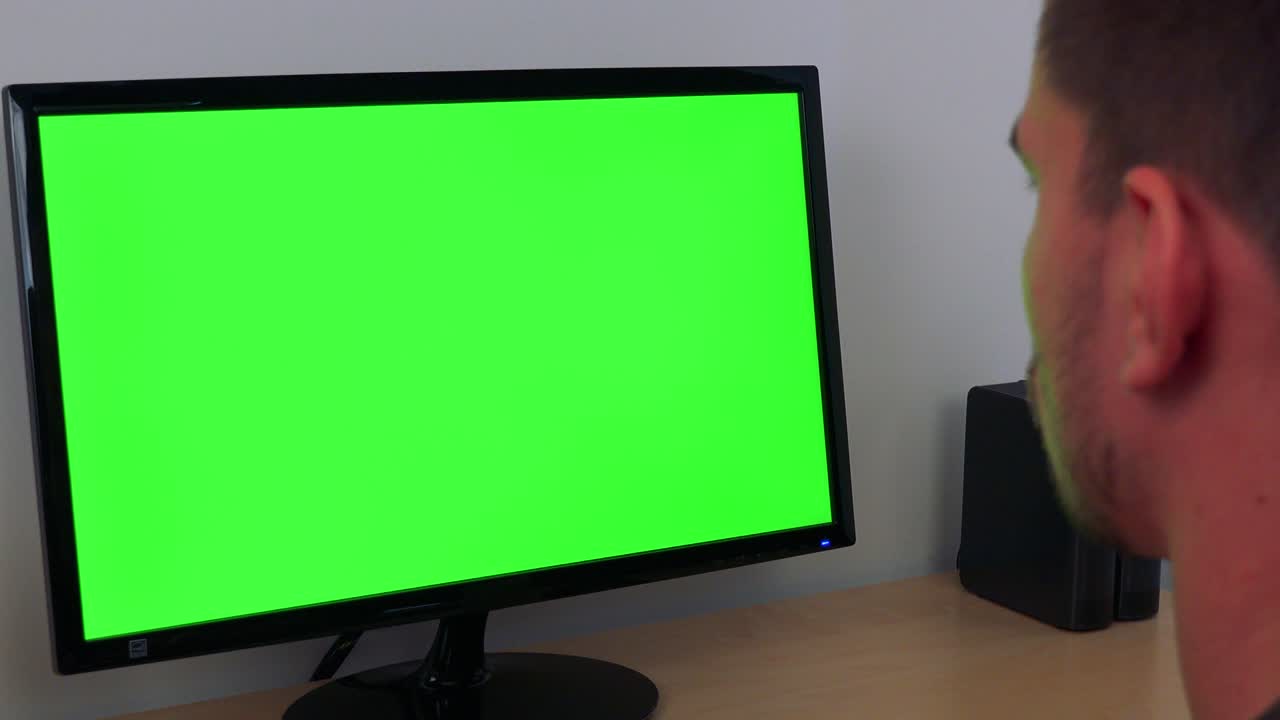 A man looks at a computer with a green screen