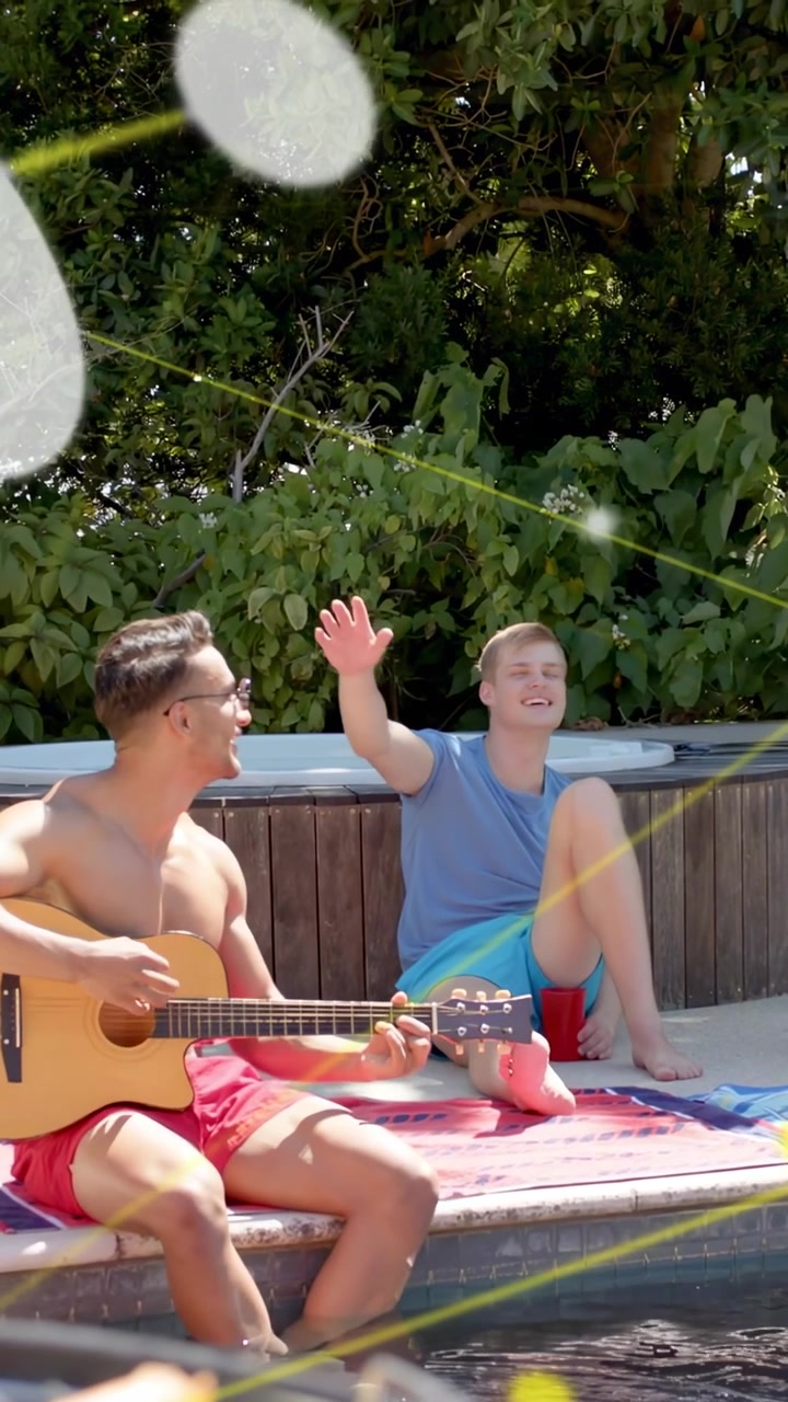 Vertikales Video: Männer spielen Gitarre am Pool, während ein Freund außerhalb des Bildes winkt und den Kopf anlehnt, Lens Flares, Werbung.