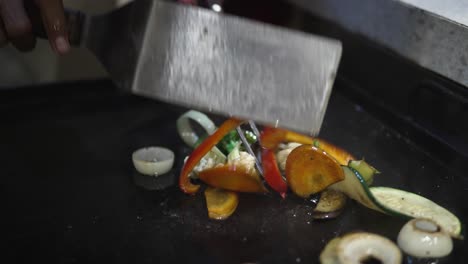 chef man cooking stir frying, mixing vegetables on grill - hands close-up slow motion