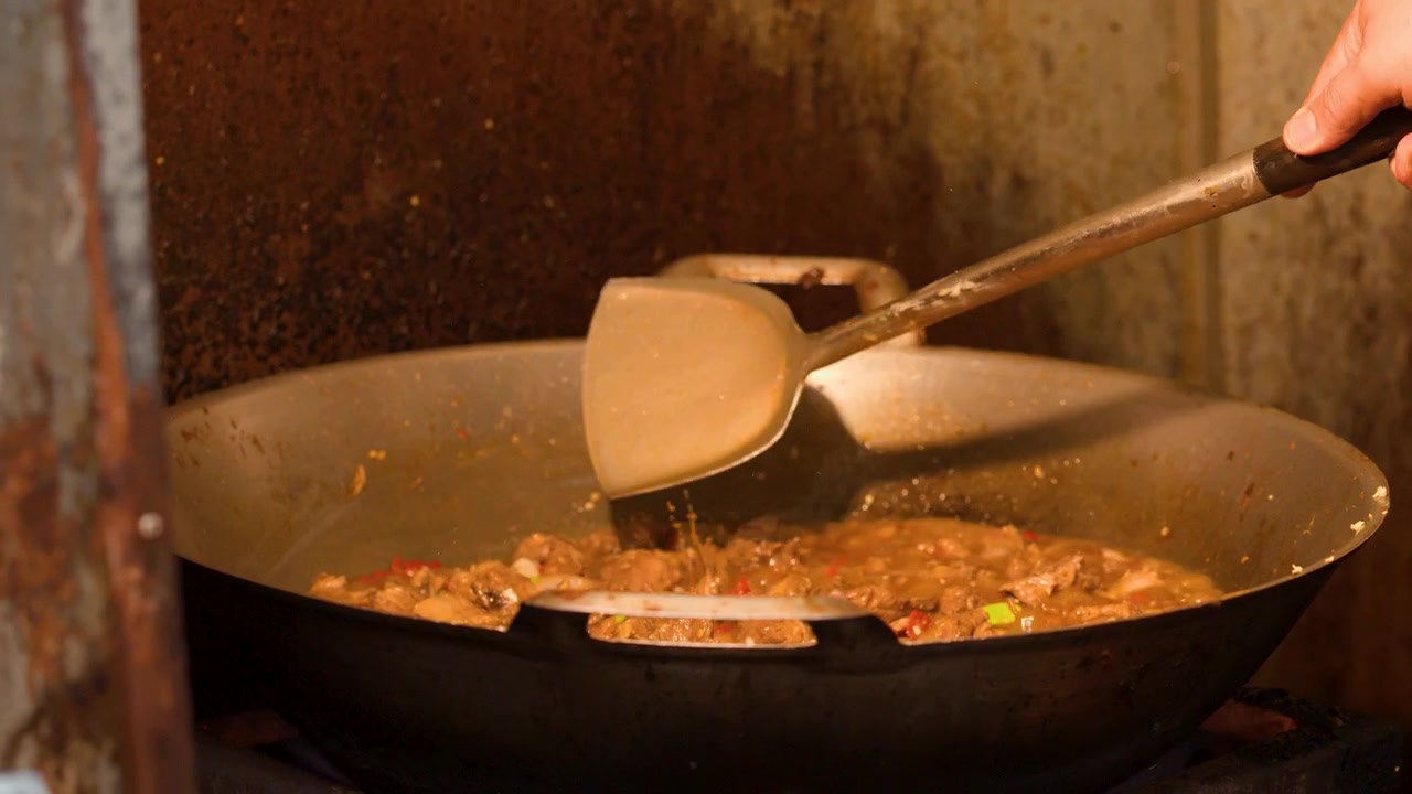 Primo piano di uno chef che mescola carne e verdure in un grande wok sul fuoco